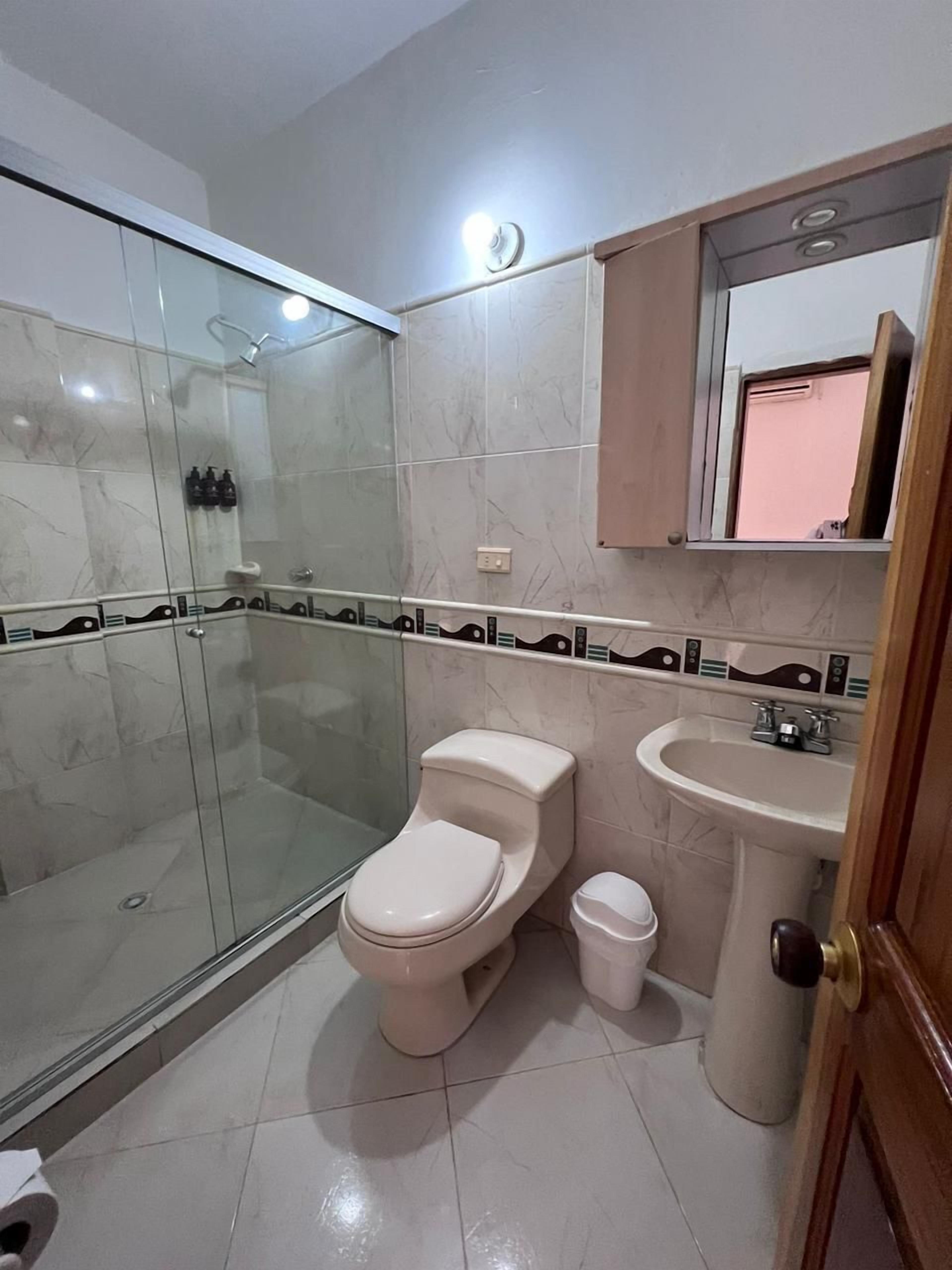 Un baño con ducha de mampara de vidrio, inodoro, lavabo y espejo sobre el lavabo.