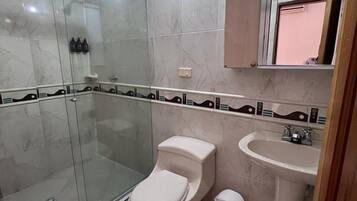 Un baño con ducha de mampara de vidrio, inodoro, lavabo y espejo sobre el lavabo.