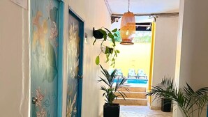 Un pasillo con dos puertas, cada una decorada con motivos florales, que conducen a una habitación. Hay plantas en macetas a lo largo del pasillo y una lámpara colgante arriba.