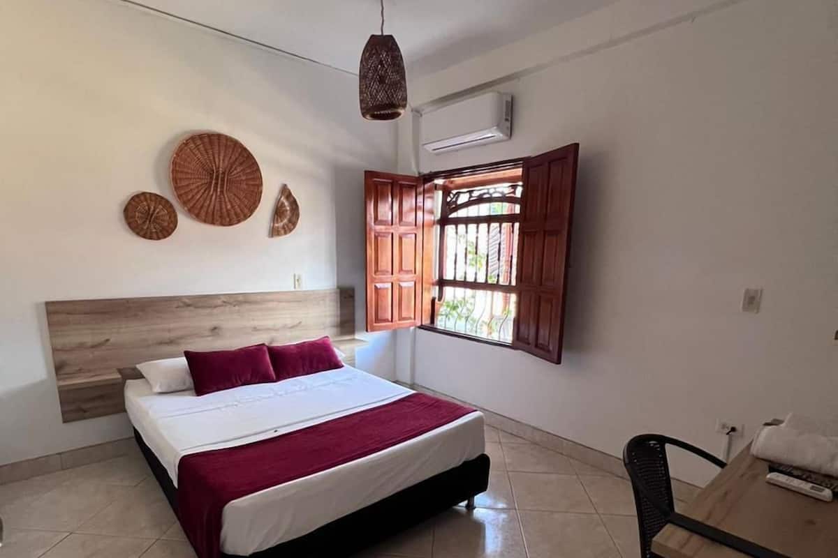Un dormitorio con cama, escritorio y ventana con contraventanas abiertas.