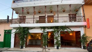 Un edificio de dos pisos con balcón, plantas en macetas y un letrero en un idioma extranjero.