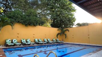 Piscina com espreguiçadeiras e uma parede amarela.