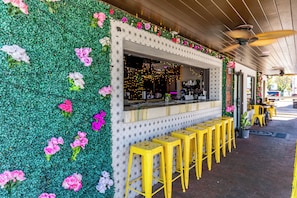 A restaurant with a green wall adorned with flowers, a counter with stools, and a ceiling fan.