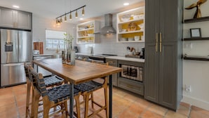 A modern kitchen with stainless steel appliances, wooden dining table, and grey cabinetry. - Gorgeously Updated NSB Getaway with View of the Ebbing Tide and Pool (New Smyrna Beach)