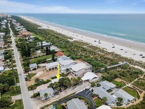 Vue aérienne d’un quartier résidentiel situé sur la côte, avec une plage, des maisons et un grand bâtiment blanc sur lequel est visible une flèche jaune pointant vers lui.
