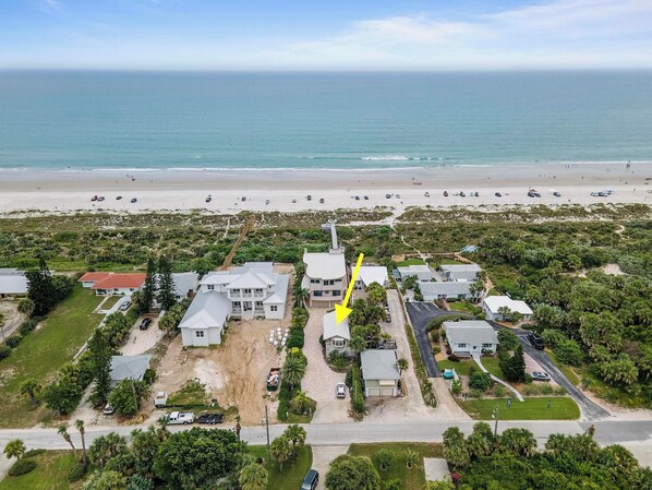 Vue aérienne d’une zone résidentielle côtière, avec des maisons, une plage et un ciel dégagé.
