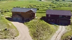 Dos casas rurales con garajes adosados, rodeadas de campos abiertos y un camino de tierra.
