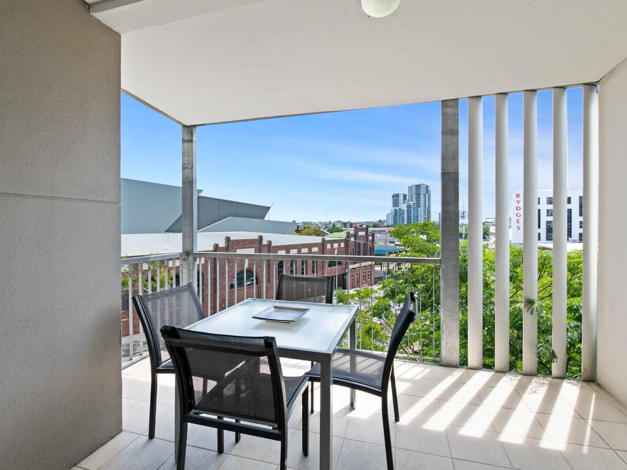 A balcony with a table and chairs, a view of buildings, and a clear sky.