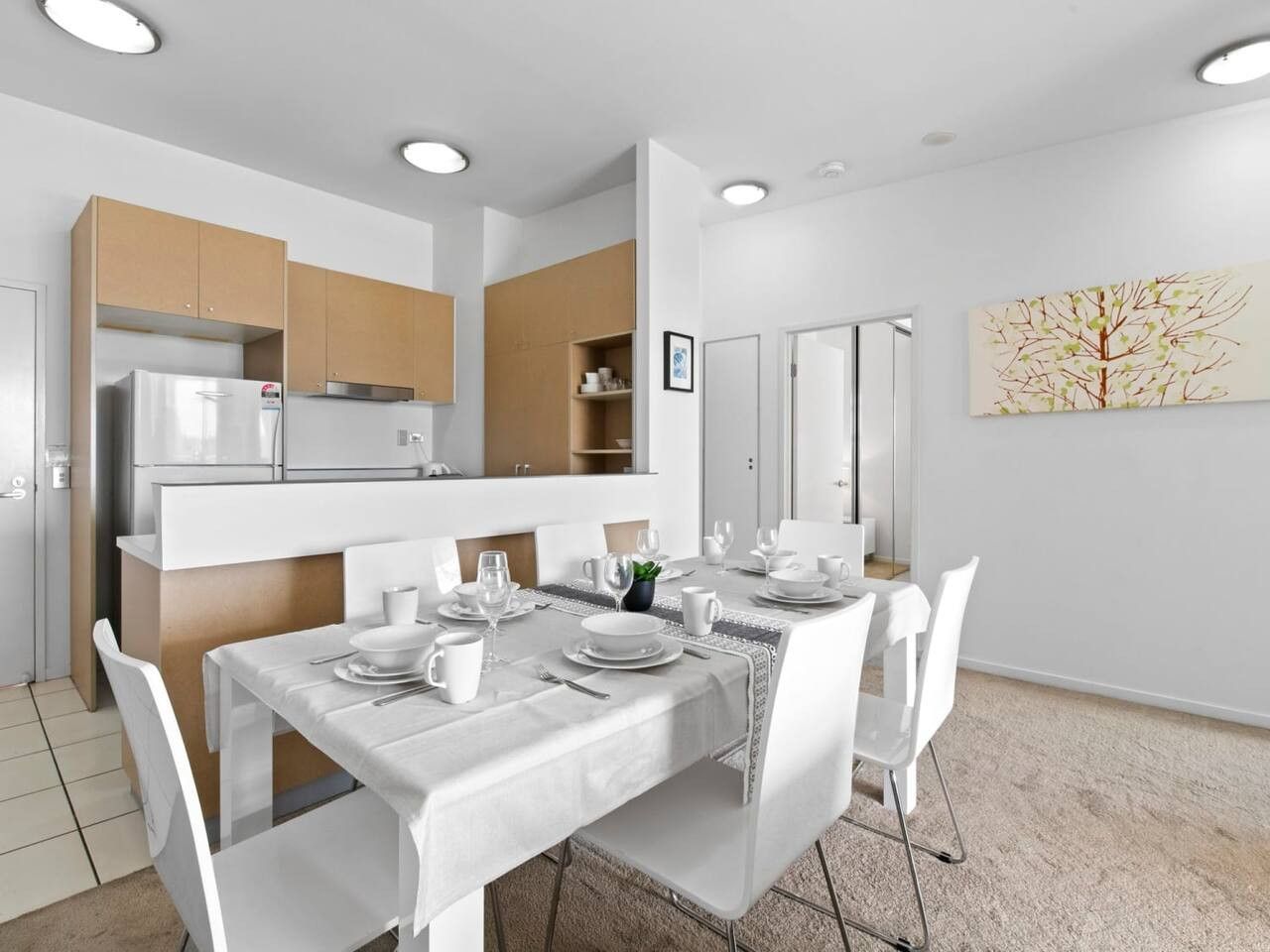 A modern dining area with a white table set for four, surrounded by white chairs.
