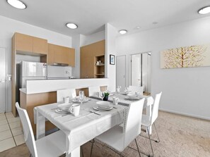 Un espace repas moderne avec une table blanche dressée pour quatre personnes, entourée de chaises blanches.