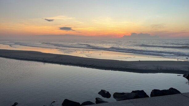 A beach with calm waters and a sunset in the background.