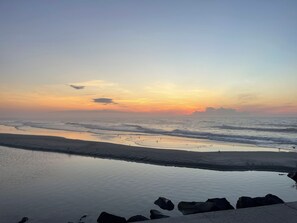 Una playa con aguas tranquilas y un atardecer de fondo.