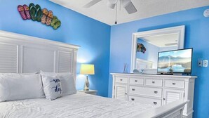 A bedroom with a white bed, a dresser, a mirror, and a TV.