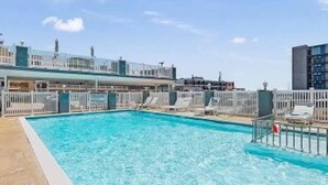 A rooftop pool with clear blue water, surrounded by white railings and lounge chairs.