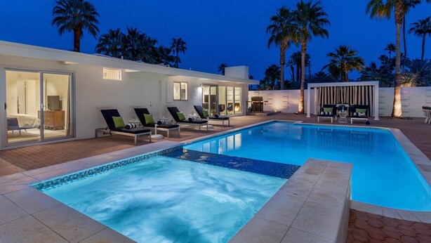 A modern pool area with lounge chairs, a swimming pool, and palm trees.