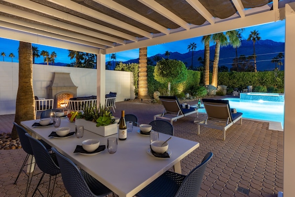 Un patio exterior con una mesa lista para comer, una parrilla, sillas de descanso y una piscina.