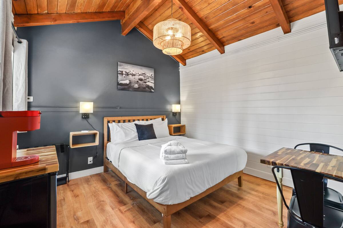 A bedroom with a wooden bed, bedside tables, a red coffee maker, a wall-mounted picture, and a window with blinds.