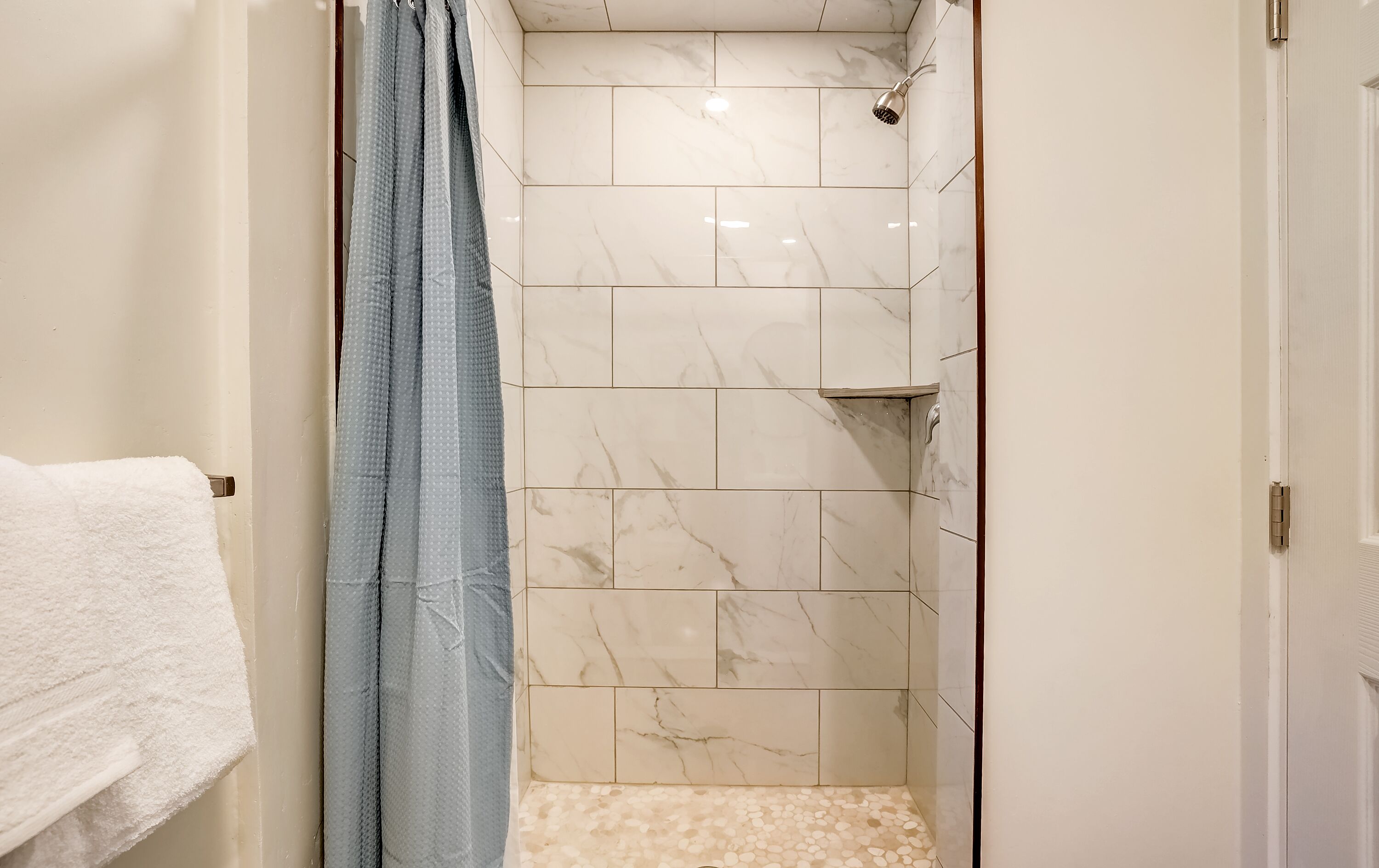 Un baño con ducha, paredes de azulejos y una toalla blanca en un perchero.