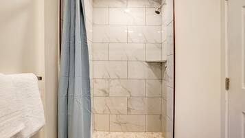 Un baño con ducha, paredes de azulejos y una toalla blanca en un perchero.