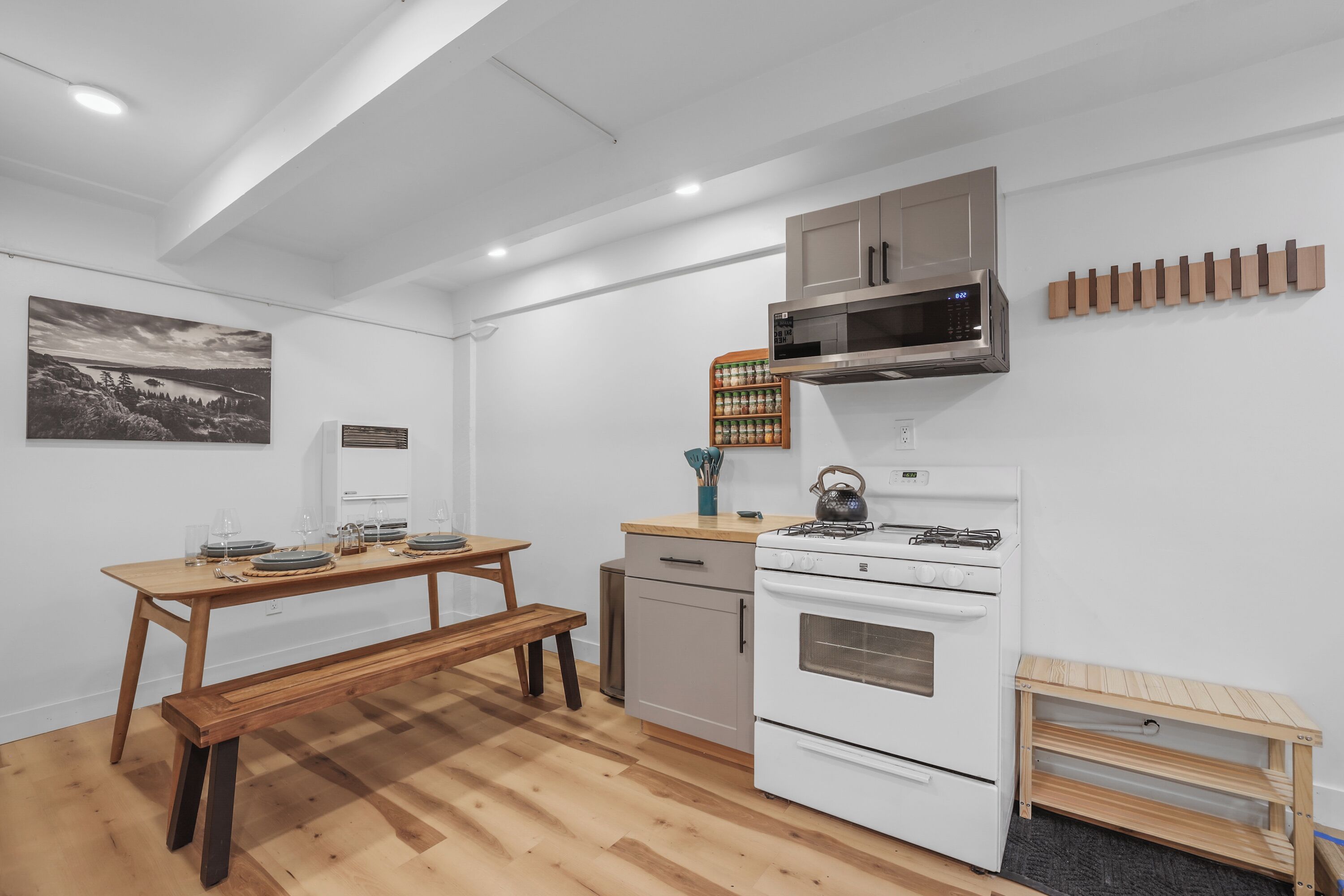 A compact kitchen with a wooden table, bench, white appliances, and a wall-mounted rack.