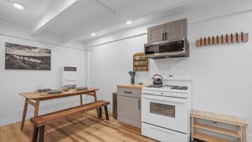 A compact kitchen with a wooden table, bench, white appliances, and a wall-mounted rack.