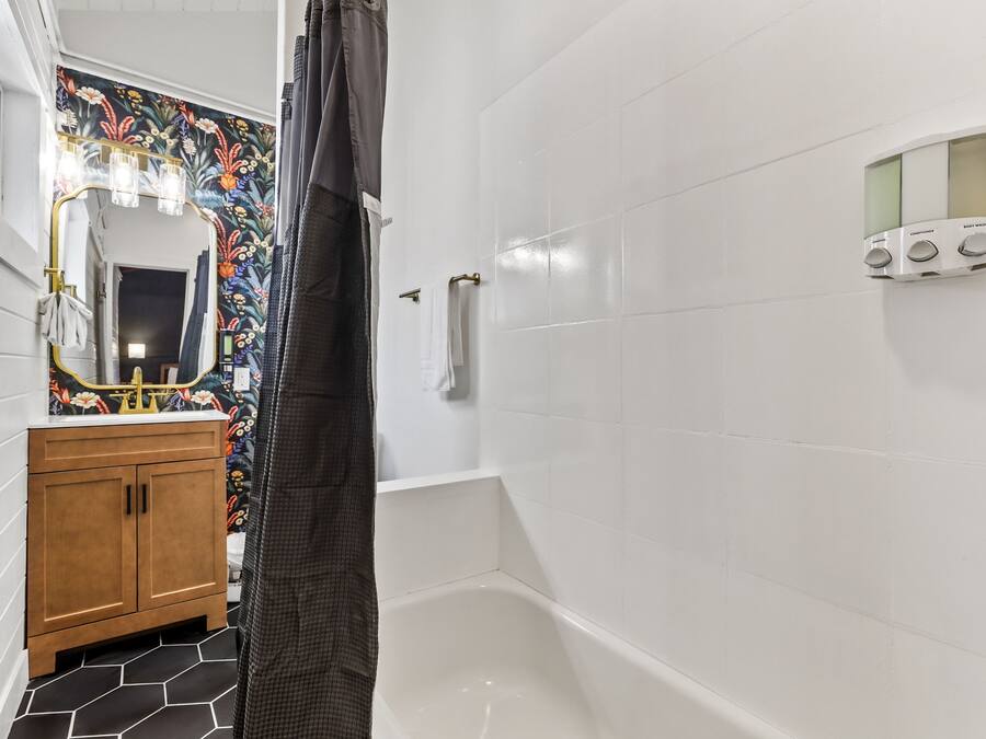 Un bagno con parete rivestita in piastrelle bianche, un mobile lavabo in legno con specchio, una tenda per la doccia e un pannello a parete per controllare la temperatura e il flusso dell'acqua.