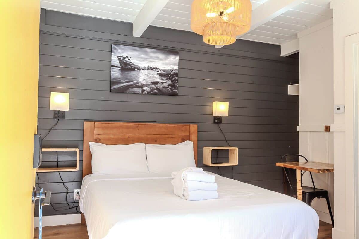 A neatly made bed with white linens, a wooden headboard, and a wall-mounted picture of a rocky landscape.