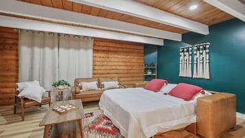 A cozy room with a wooden ceiling, a bed with white and red bedding, a brown leather sofa, a wooden coffee table, and a patterned rug.