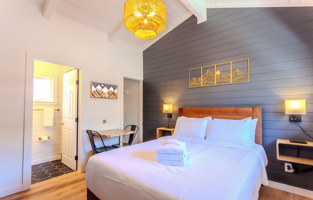 Un dormitorio con una cama grande, mesitas de noche, un escritorio y una silla. Hay una puerta que da a otra habitación.