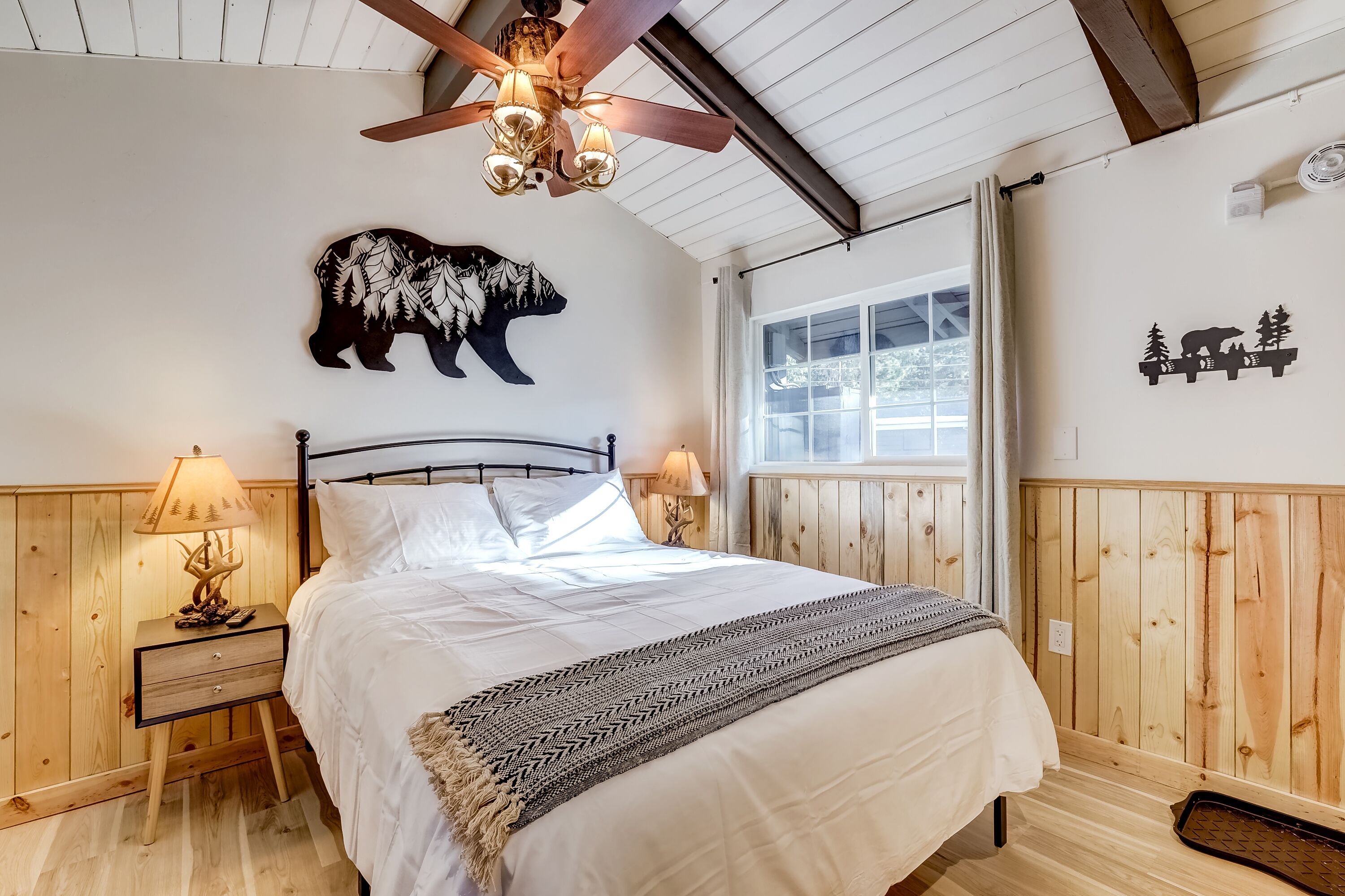 A bedroom with a bed, wooden walls, a ceiling fan, and a window.