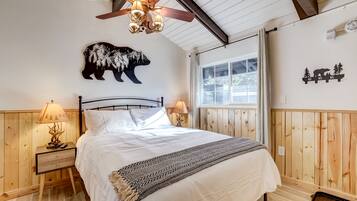 A bedroom with a bed, wooden walls, a ceiling fan, and a window.