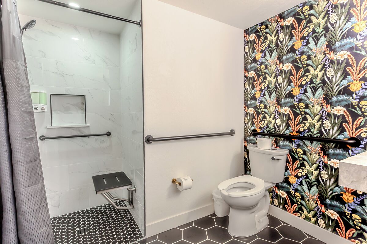 Une salle de bain avec une douche à parois de verre, des toilettes et un mur décoré d’un motif.