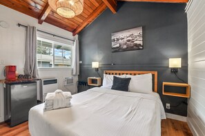 A modern hotel room with a large bed, a small kitchenette, a window with curtains, a wall-mounted picture, and a ceiling light fixture. - Tahoe Mountain inn (South Lake Tahoe)