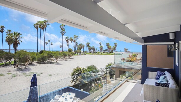 A balcony with a view of the beach, palm trees, and a clear sky.
