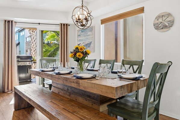 A dining area with a wooden table set for six, a vase with sunflowers, and a view of the outside.