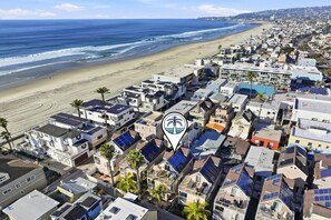 A coastal residential area with multiple buildings, some with solar panels, and a beach in the background.