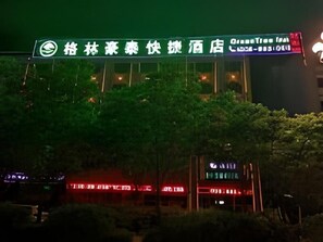 A hotel sign with illuminated text and a logo, surrounded by greenery. - Greentree Inn Jiayuguan Xinhua Nan Road (Jiayuguan)