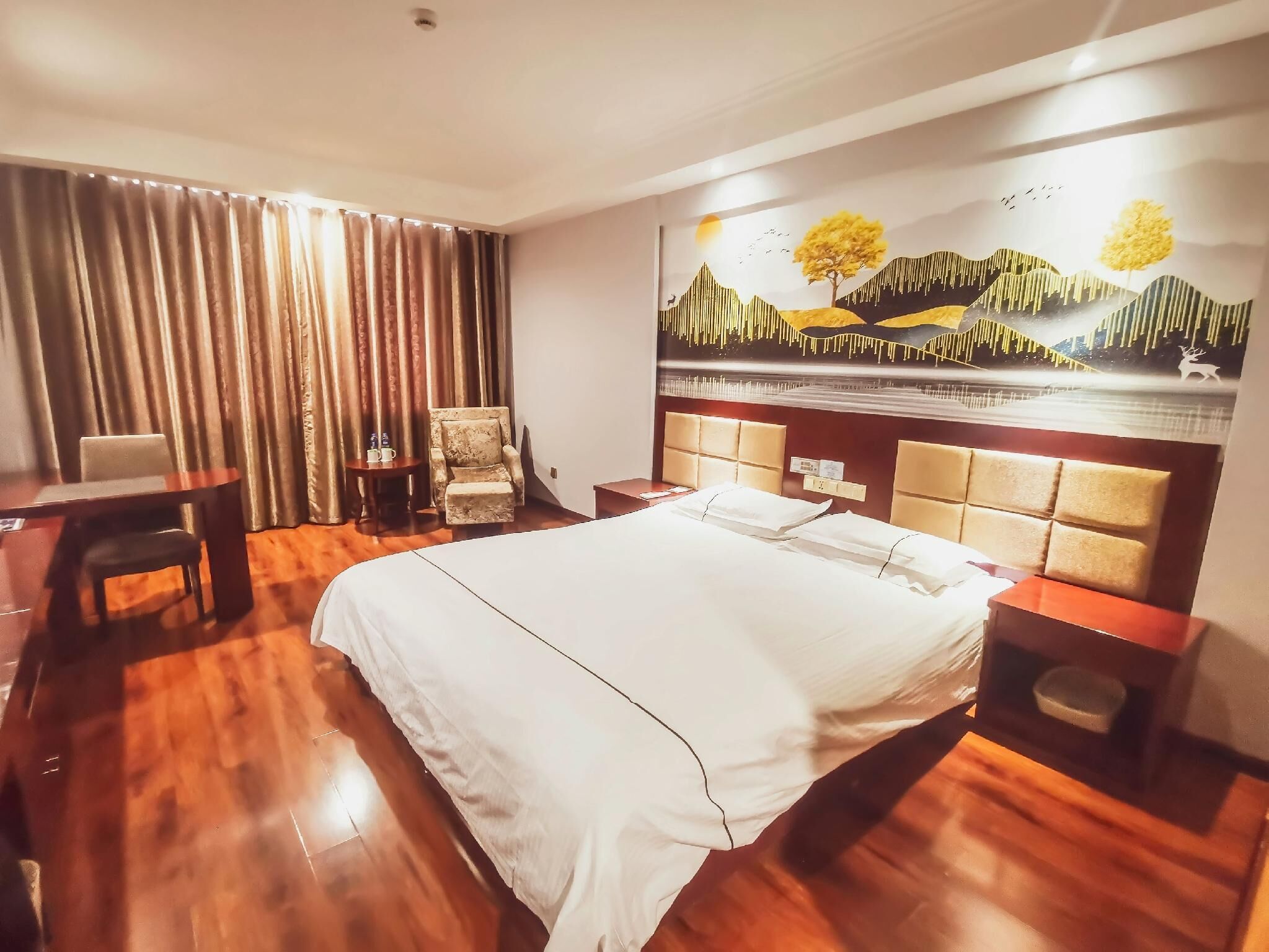 A hotel room with a large bed, a desk, a chair, and a painting on the wall.