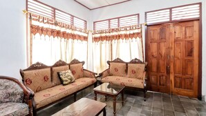 A living room with two sofas, a coffee table, and a wooden door. - Narendra Homestay by Zuzu (Sleman)