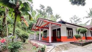 A two-story building with a red and white facade, surrounded by lush greenery and a garden with pink flowers. - Narendra Homestay by Zuzu (Sleman)