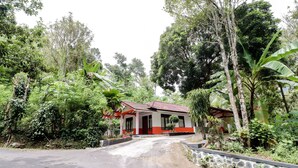 A house with a red and white exterior, surrounded by lush greenery and trees. - Narendra Homestay by Zuzu (Sleman)