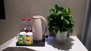 A countertop with a coffee maker, Lipton tea bags, bottled water, and a potted plant. - Shell Shanghai Wanda Square Wujiaochang Metro Station Hotel (Shanghai)