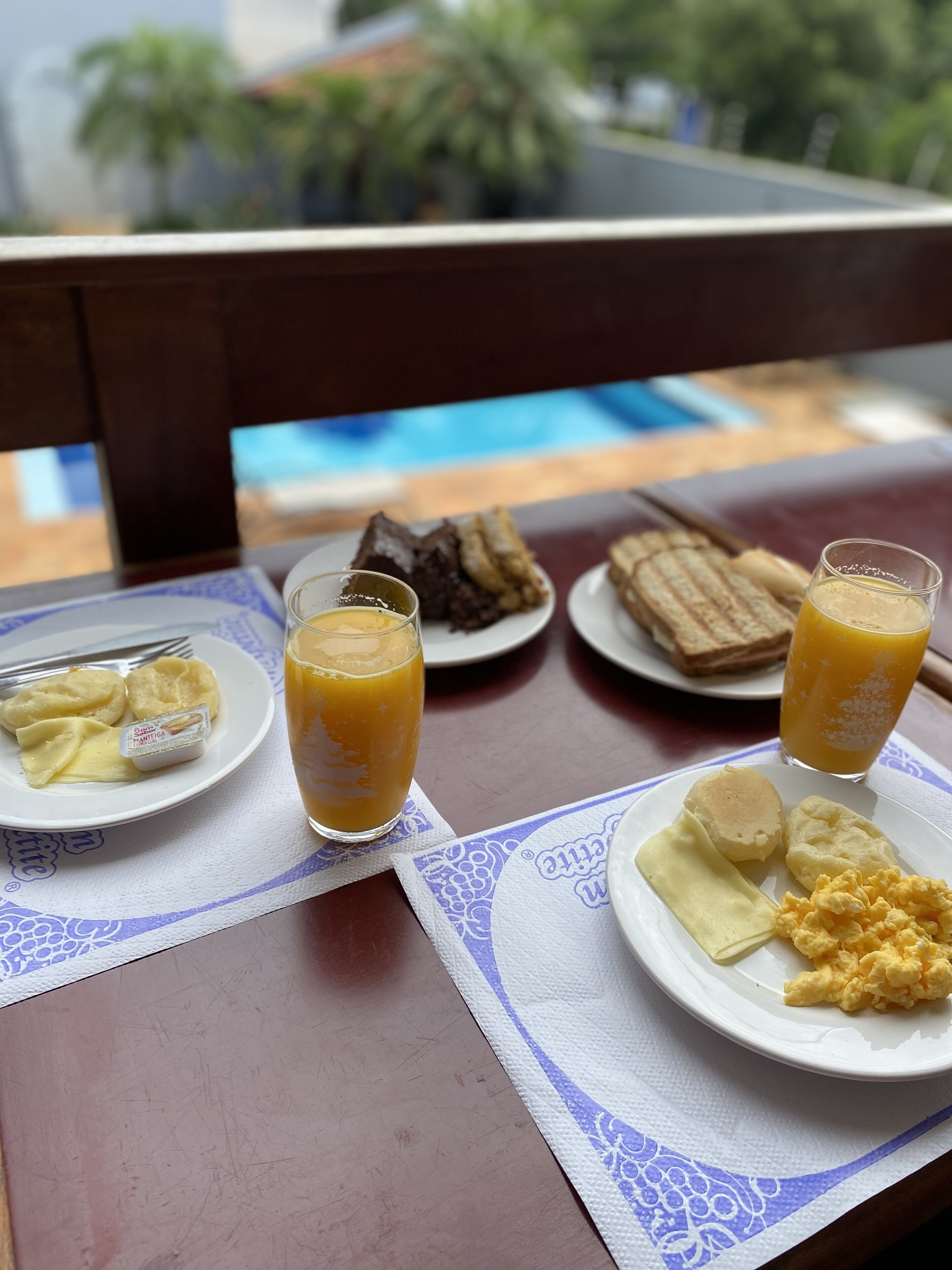 Ett bord med frukosttillbehör, inklusive äggröra, rostat bröd och juice, uppdukat på ett träbord med utsikt över grönskan i bakgrunden.