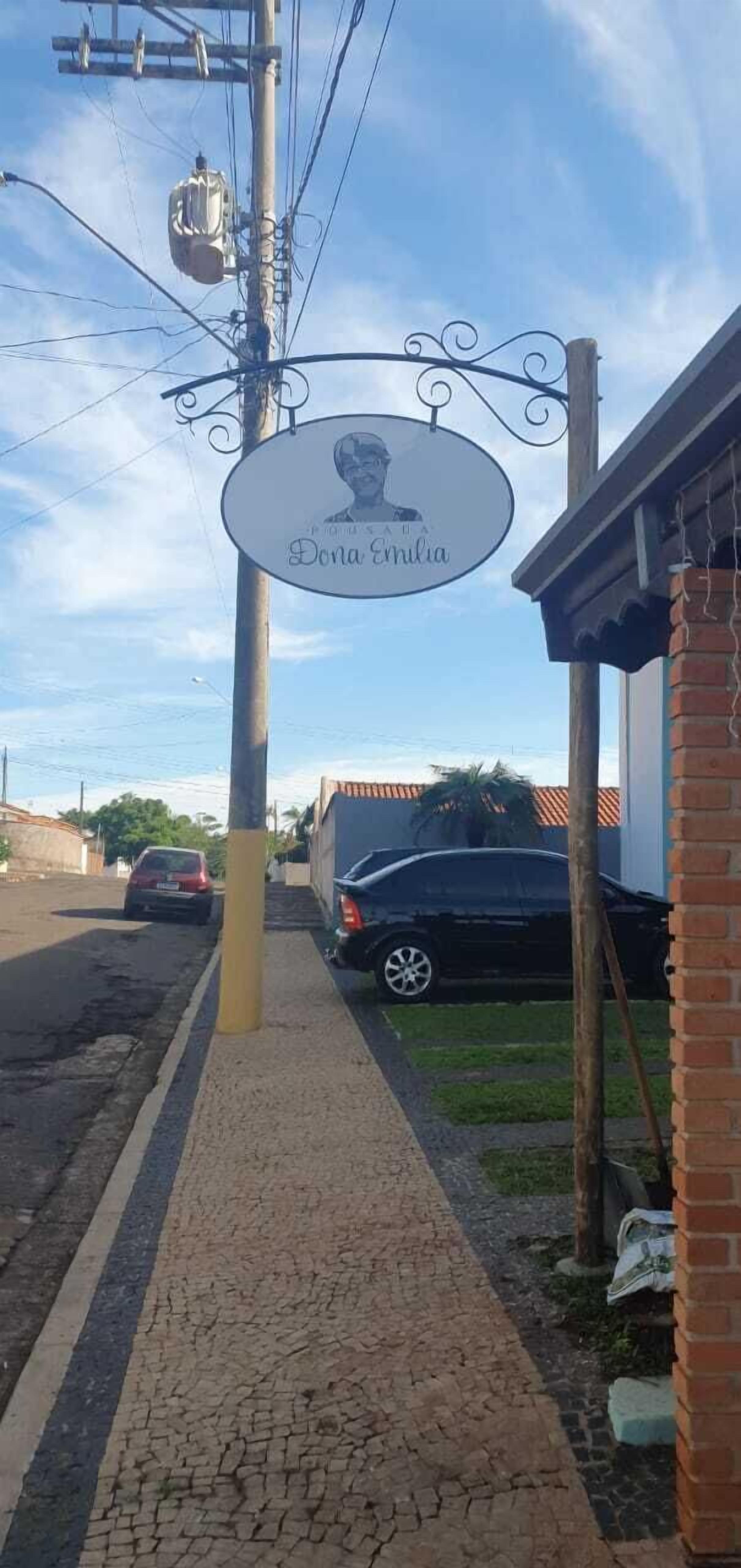 Un cartello stradale con un nome proprio, un marciapiede lastricato, un'auto parcheggiata e un edificio con tetto rosso.