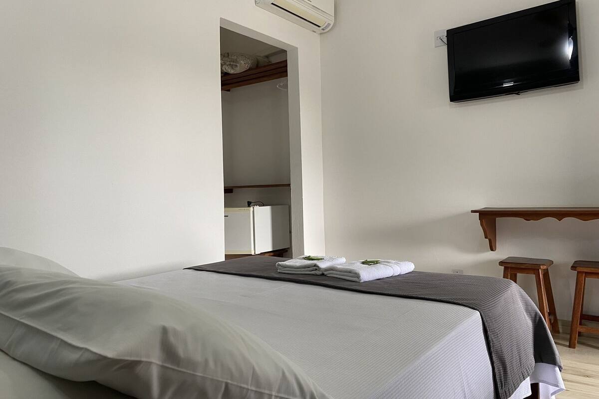 Une chambre d’hôtel équipée d’un lit, d’un téléviseur à écran plat, d’un bureau avec deux chaises et d’un appareil de climatisation.