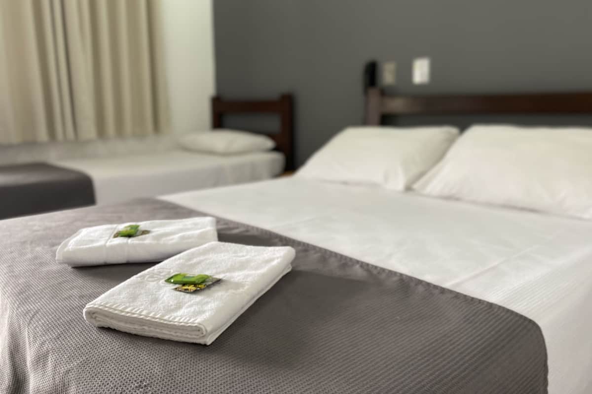 Un lit bien fait, avec du linge de lit blanc et deux serviettes pliées ornées d’un motif représentant une feuille verte.