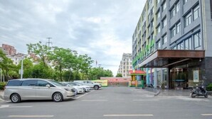 A multi-story building with a modern facade, a parking lot with several cars, and a small green structure with a red roof. - Greentree Inn Hefei Binhu New District Ziyun Road and Qingtan Road Jianghuai Car Factory (Hefei)