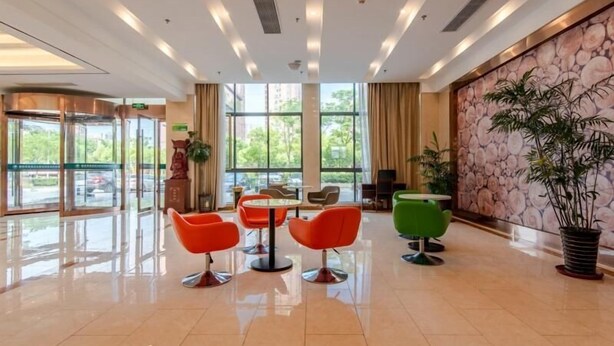 A modern lobby with a glass entrance, a central seating area with orange chairs, and a stone wall with a large potted plant. - Greentree Inn Hefei Binhu New District Ziyun Road and Qingtan Road Jianghuai Car Factory (Hefei)