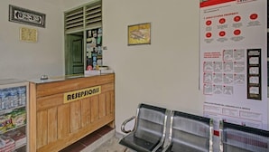 A reception area with a wooden desk labeled "RECEPTION," a clock, and a poster with health guidelines. - OYO 3724 Penginapan Baiti Jannati Syariah (Banjarbaru)