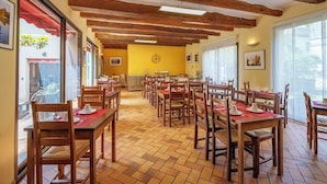 A dining area with wooden tables and chairs, a yellow wall with a clock, and large windows. - Hotel Val De Loire (Azay-le-Rideau)